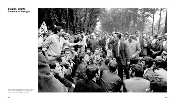 Shot of wet brick roads of Milan in rain, surrounded by buildings, CESARE COLOMBO Fotographie Photographs 1952-2012 in yellow and white font to centre right.