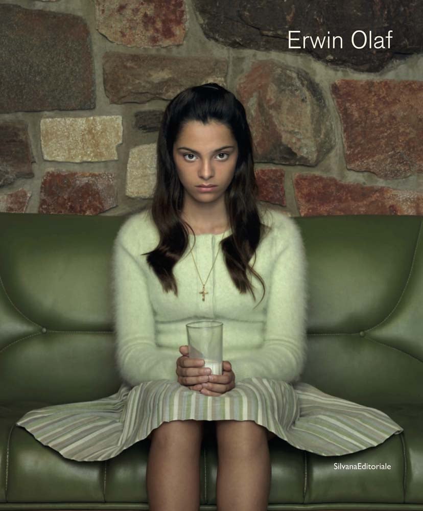 Book cover of Erwin Olaf, with a portrait photograph titled The Niece, Palm Springs, 2018, with girl sitting on green sofa holding glass of milk. Published by Silvana