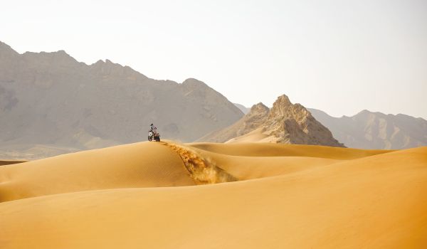 Book cover of Dream Wilder', with a Ducati DesertX off-road motorcycle with rider, speeding across a sandy desert, with sand spray behind. Published by Silvana.