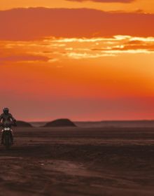 Book cover of Dream Wilder', with a Ducati DesertX off-road motorcycle with rider, speeding across a sandy desert, with sand spray behind. Published by Silvana.