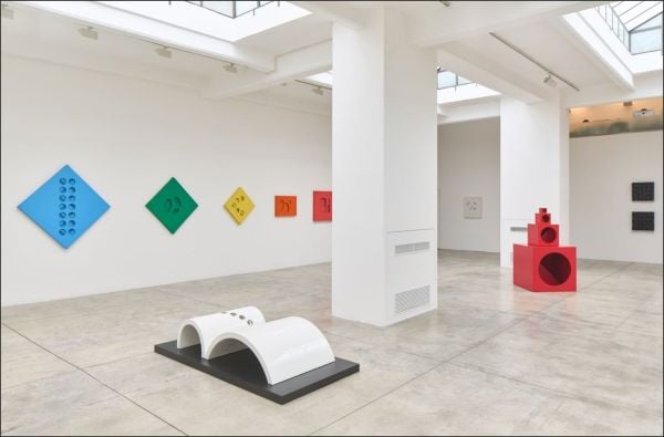 Book cover of Paolo Scheggi, with the Italian artist wearing a suit, standing in a studio surrounded by his elliptical holed canvases. Published by Silvana.