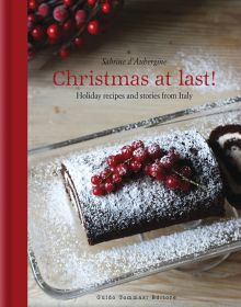 Christmas chocolate roulade, sprinkled with icing sugar, on glass dish, on cover of 'Christmas at Last! Holiday Recipes and Stories from Italy', by Guido Tommasi Editore.