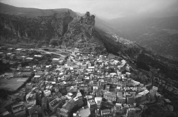 Book cover of Legarsi alla Montagna, Binding to the mountain, featuring a woman in black, stretching out a long blue ribbon through a street. Published by 5 Continents Editions.