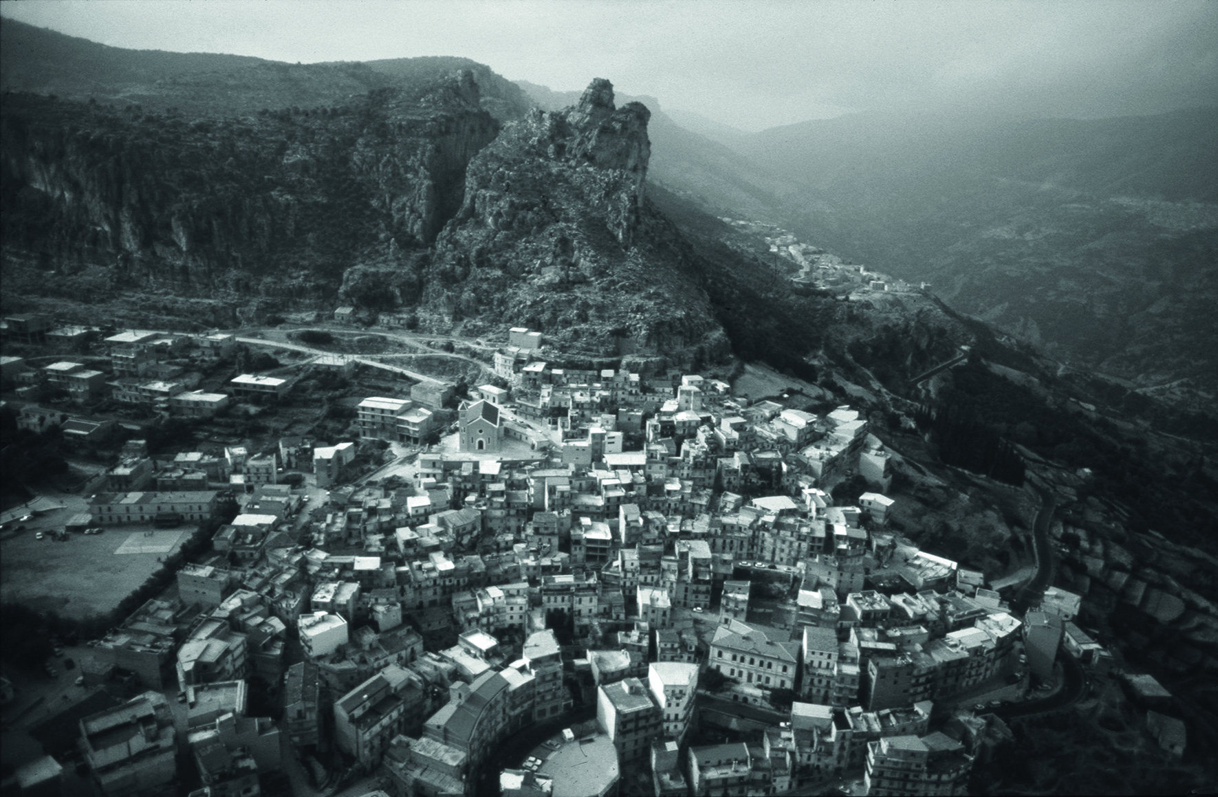 Book cover of Legarsi alla Montagna, Binding to the mountain, featuring a woman in black, stretching out a long blue ribbon through a street. Published by 5 Continents Editions.