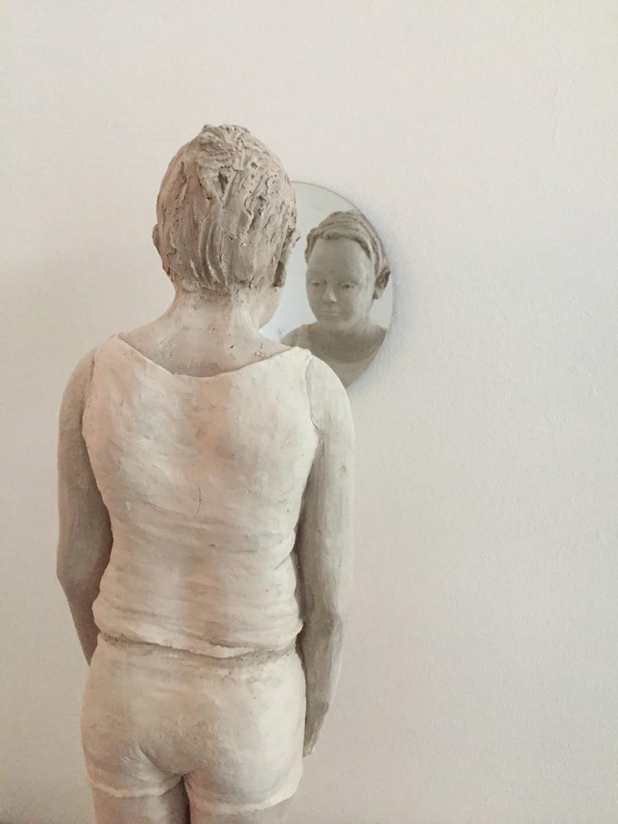 Life sized clay sculpture of girl sitting on bed, Breath in pale grey font above