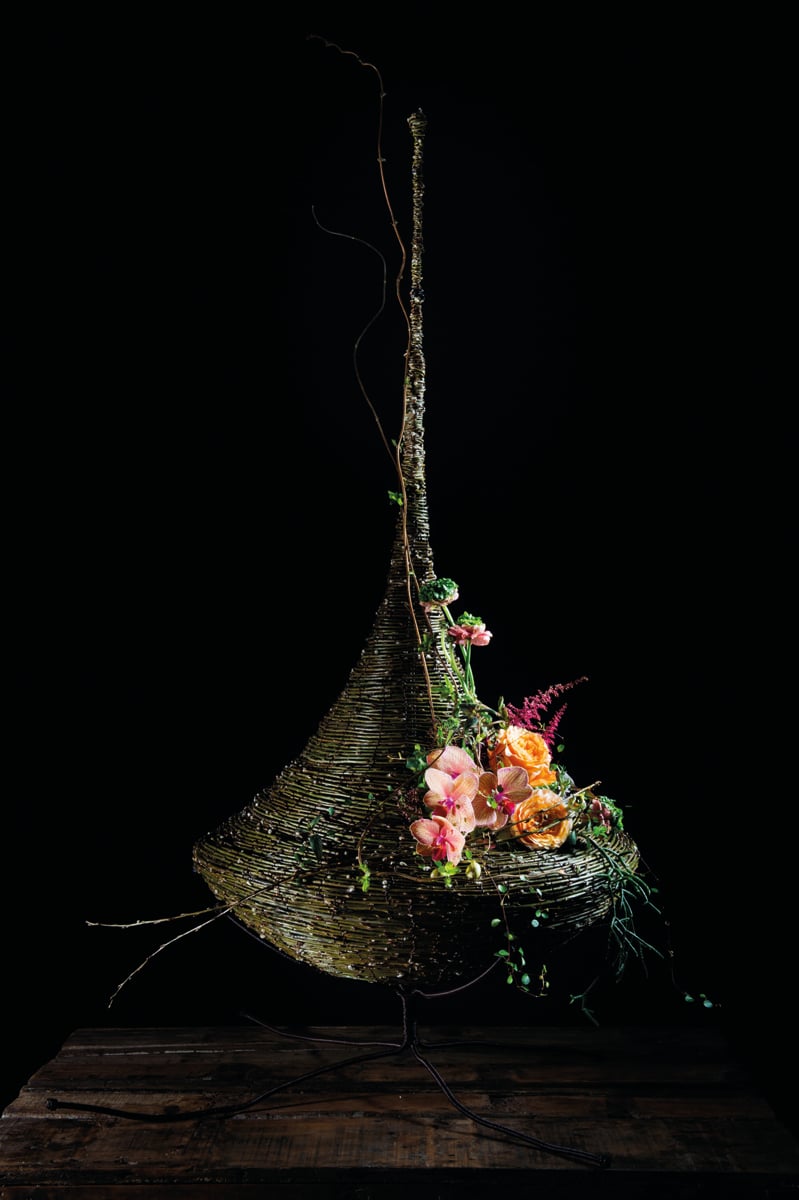 White book cover of International Floral Art 2018/2019, with a model wearing white face paint, and a head-dress of white flowers cascading down. Published by Stichting.