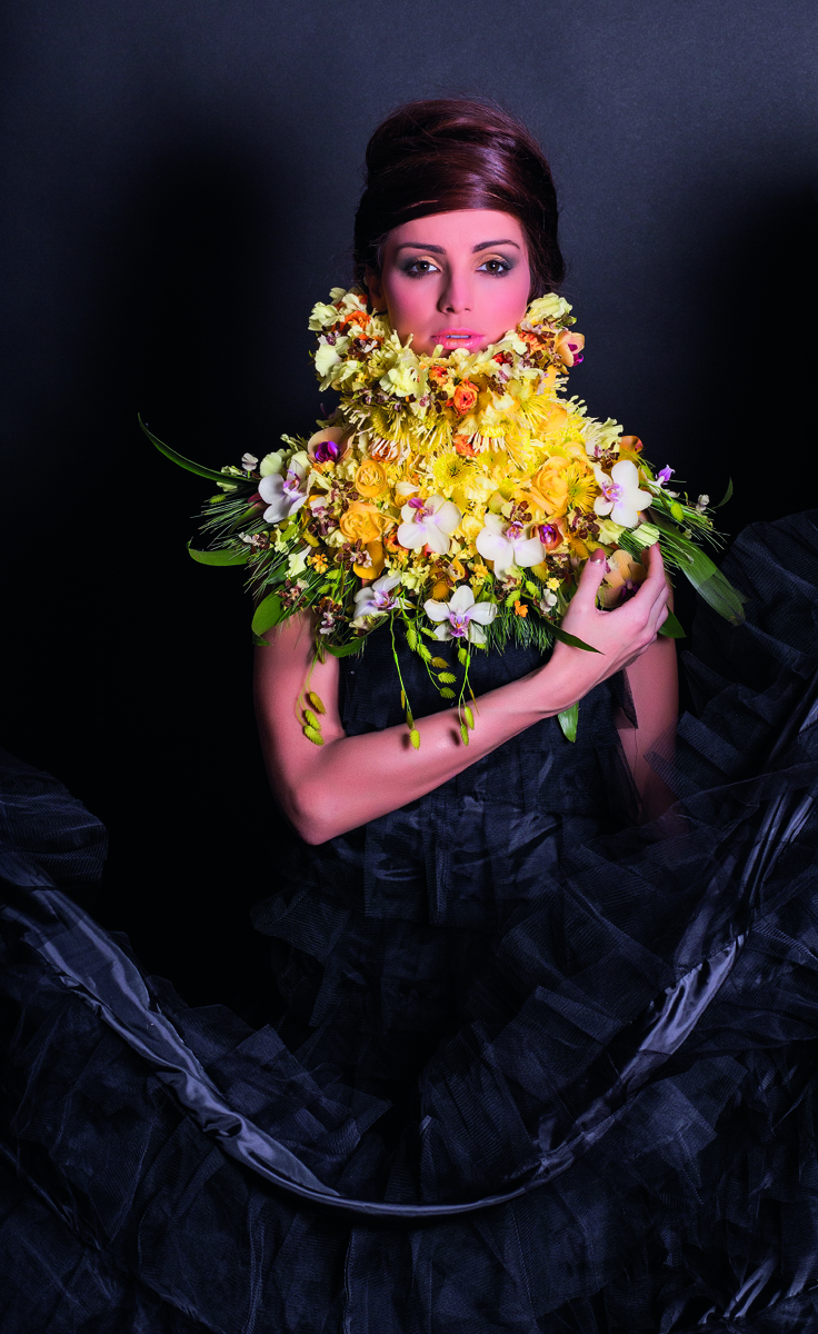 White book cover of International Floral Art 2018/2019, with a model wearing white face paint, and a head-dress of white flowers cascading down. Published by Stichting.