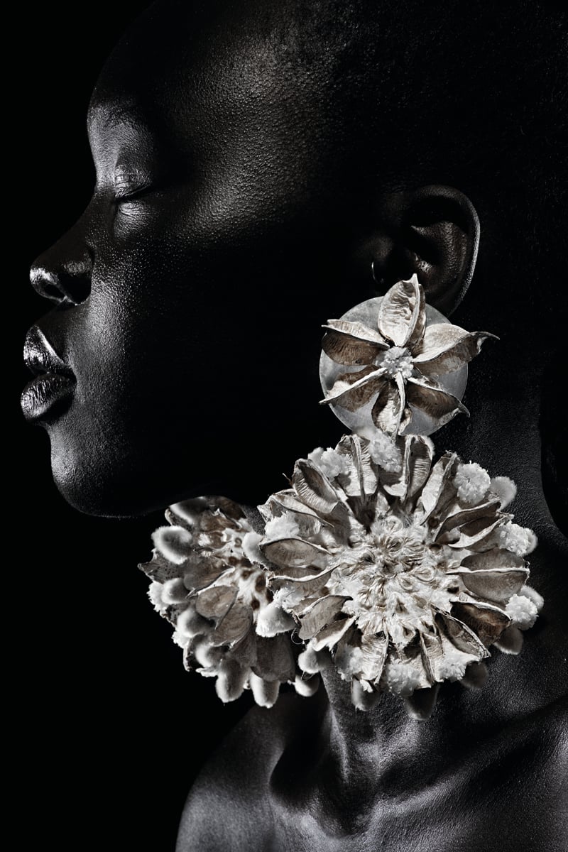 White book cover of International Floral Art 2018/2019, with a model wearing white face paint, and a head-dress of white flowers cascading down. Published by Stichting.