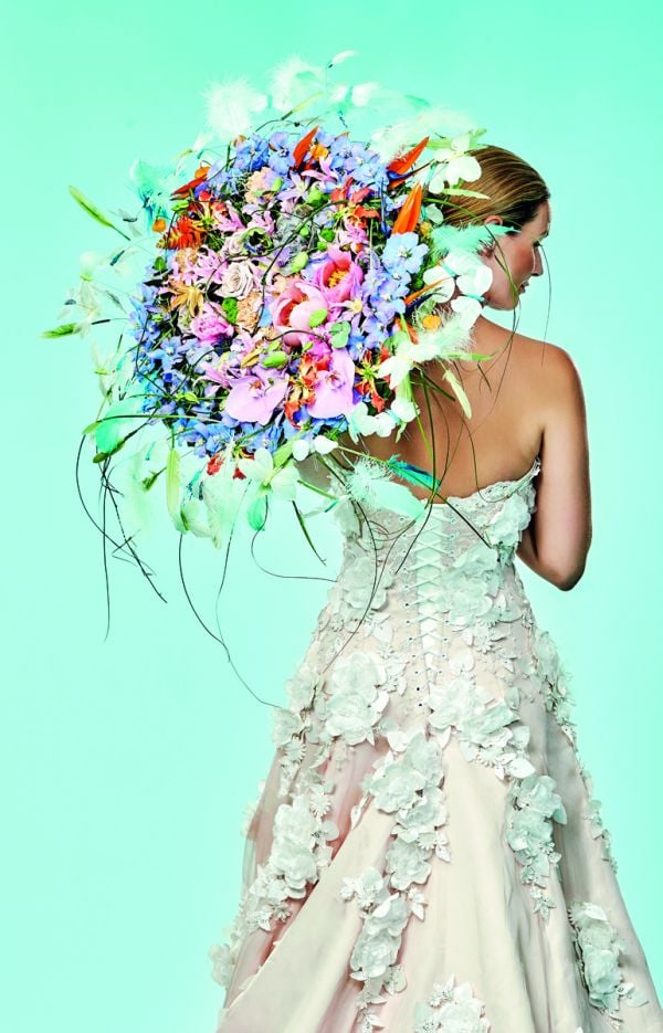 Book cover of The World of Colour According to Per Benjamin, with a model wearing a ring of pink and yellow lilies around neck, with long thin feathers spraying out. Published by Stichting.
