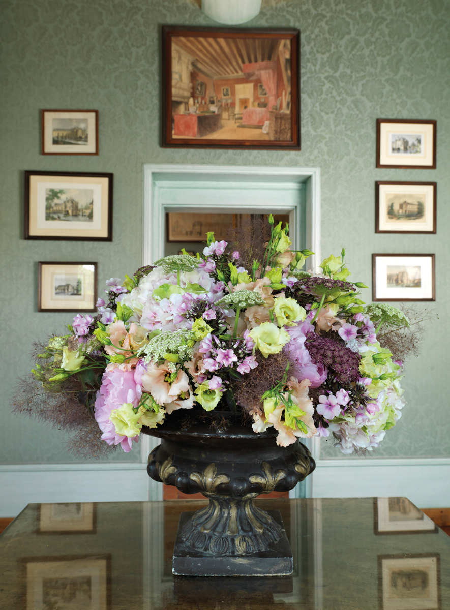 Bouquet of flowers in urn with base, in front of decorative fireplace, THE BOUQUETS OF CHENONCEAU in bright yellow font above.