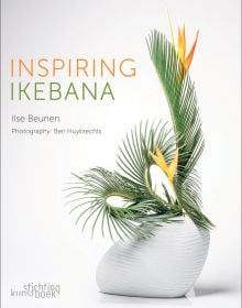 Book cover of Inspiring Ikebana, featuring an ceramic vase with three long green palm leaves and two bird of paradise flowers. Published by Stichting.