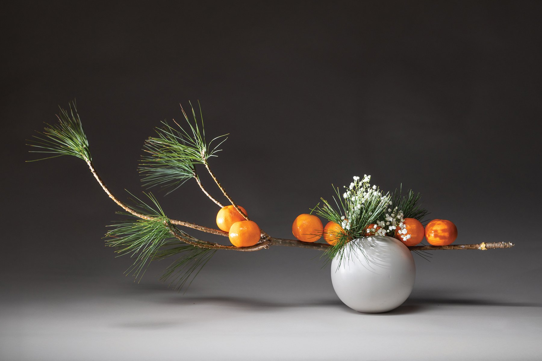 Book cover of Inspiring Ikebana, featuring an ceramic vase with three long green palm leaves and two bird of paradise flowers. Published by Stichting.