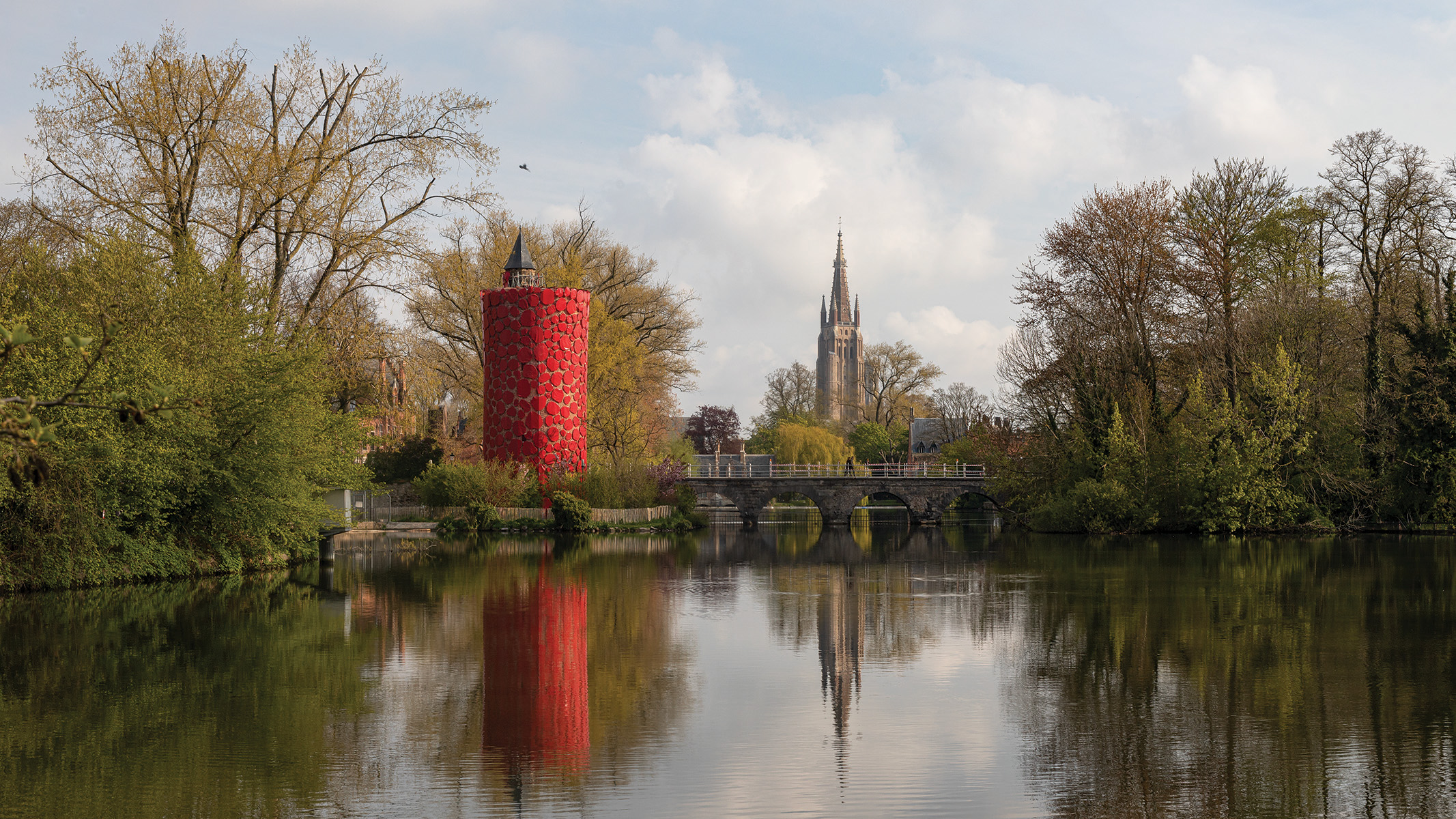 Book cover of Bruges Triennial 2021, TraumA, with a red skeletal platform structure surrounded by green trees. Published by Stichting.