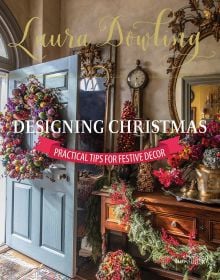 Book cover of Laura Dowling Designing Christmas: Practical Tips for Festive Decor, with an interior hallway with a large floral wreath on the door, Published by Stichting Kunstboek.