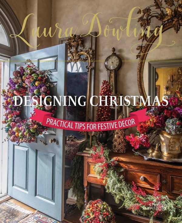 Book cover of Laura Dowling Designing Christmas: Practical Tips for Festive Decor, with an interior hallway with a large floral wreath on the door, Published by Stichting Kunstboek.
