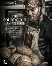 Book cover of The Sourdough Baking Book: From Sourdough Starter to Stunning Breads and Pastries; featuring a baker holding a tray of loaves of bread. Published by Lannoo Publishers.