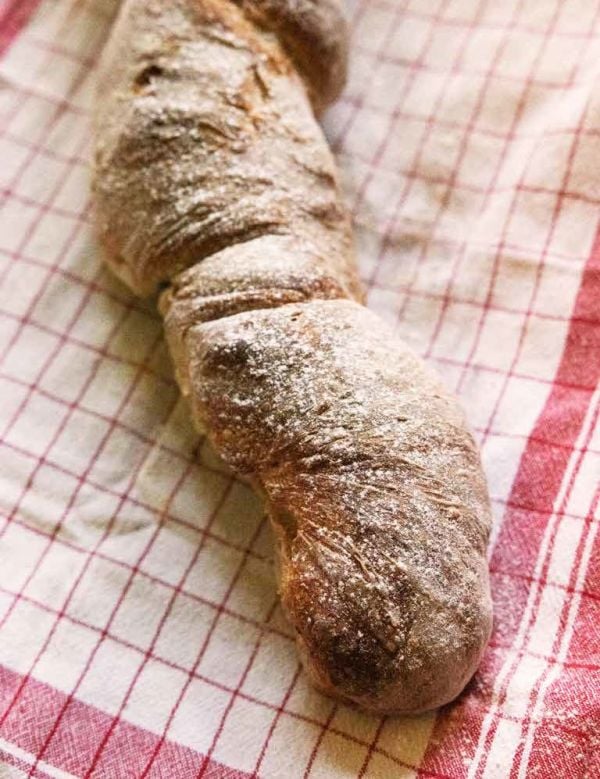 Book cover of The Sourdough Baking Book: From Sourdough Starter to Stunning Breads and Pastries; featuring a baker holding a tray of loaves of bread. Published by Lannoo Publishers.