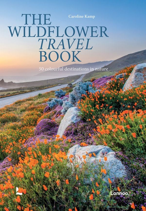 Book cover of The Wildflower Travel Book: 50 Colourful Destinations in Nature; featuring a vibrant coastal scene with blooming orange and purple wildflowers along a winding road. Published by Lannoo Publishers.