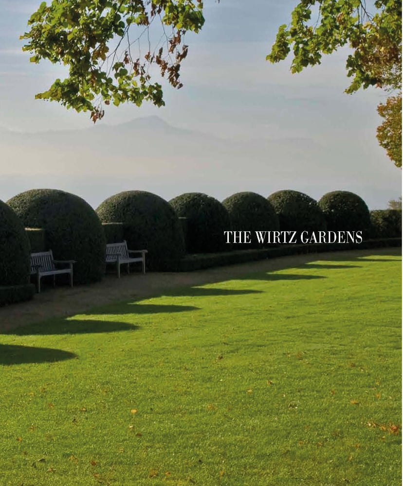 Large green topiary balls edging grass area, with 2 wooden benches, THE WIRTZ GARDENS in white font right of centre