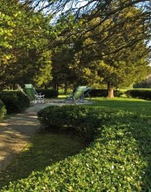 Large green topiary balls edging grass area, with 2 wooden benches, THE WIRTZ GARDENS in white font right of centre