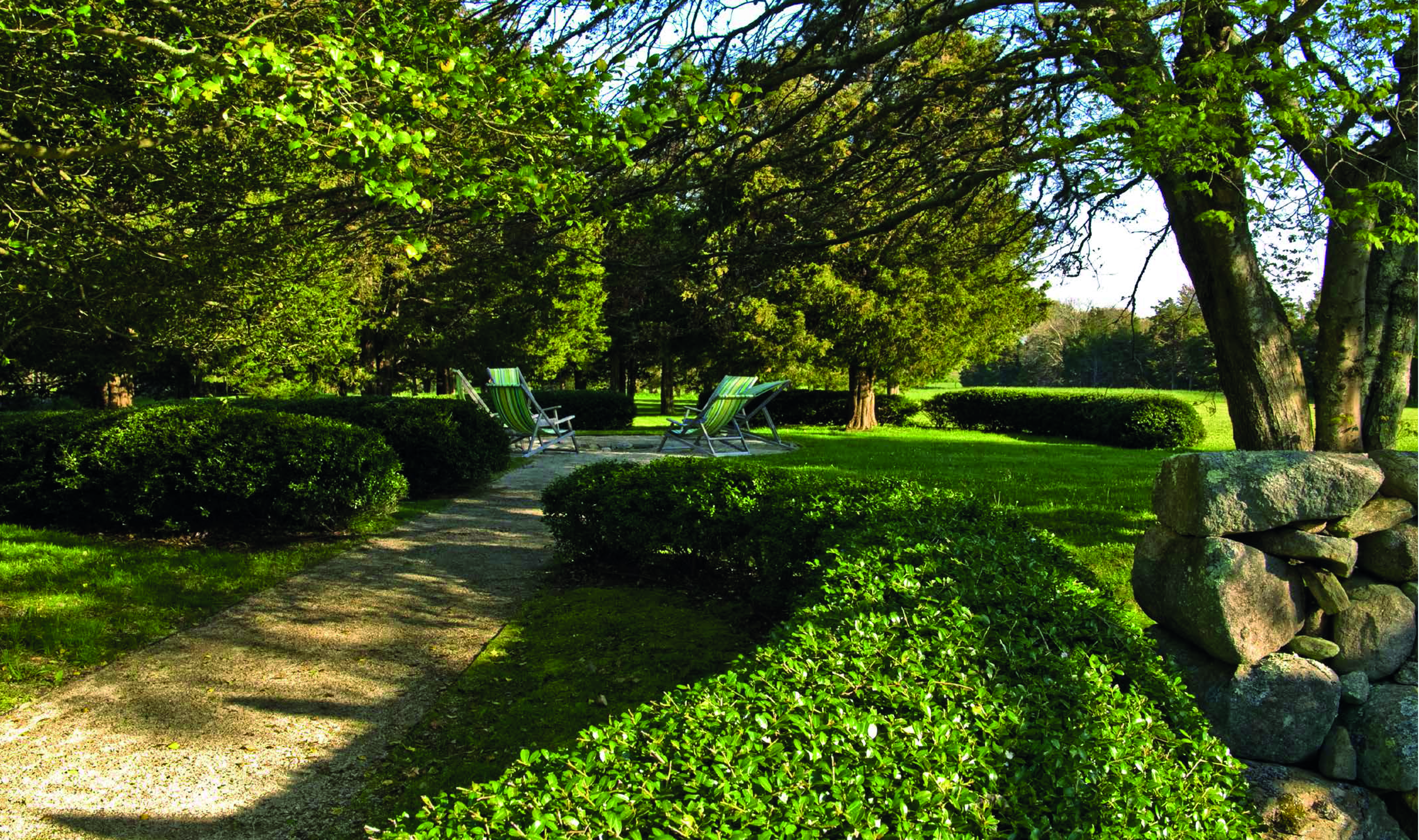 Large green topiary balls edging grass area, with 2 wooden benches, THE WIRTZ GARDENS in white font right of centre