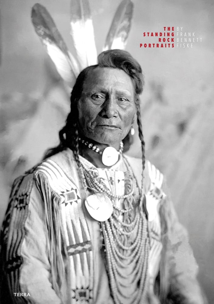Black and white shot of Fort Yate Native American tribesman, feather in hair, beads around neck, THE STANDING ROCK PORTRAITS in red font to upper right.