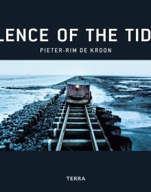 Rail road and embankment on Wadden Sea, wagon with lamp on front, on black cover of 'Silence of the Tides', by Lannoo Publishers.