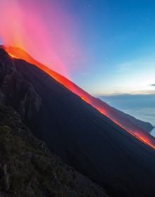 Spectacular shot of volcano spewing bright white and orange lava, LIVING WITH VOLCANOES in white font to centre.