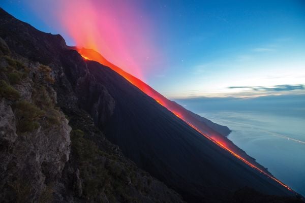 Book cover of Living With Volcanoes, with a spectacular shot of volcano spewing bright orange lava. Published by Lannoo Publishers.