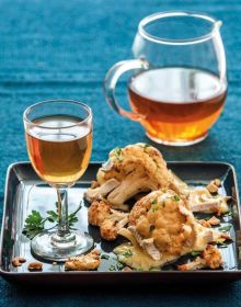 Green tea leaves on pale blue plate, deep blue tablecloth beneath, on cover of 'Tea', Wine's Sober Sibling', by Lannoo Publishers.