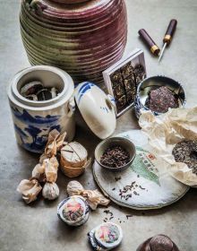 Green tea leaves on pale blue plate, deep blue tablecloth beneath, on cover of 'Tea', Wine's Sober Sibling', by Lannoo Publishers.