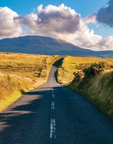 Book cover of Sabine de Milliano's, On the Road in Europe: Unforgettable Scenic Road Trips, featuring a mountainous landscape with waterfall, and winding roads below. Published by Lannoo Publishers.