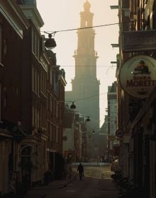 Book cover of A New Light on Amsterdam, with a misty view of a canal, and a bird flapping its wings while perched on a post. Published by Lannoo Publishers.