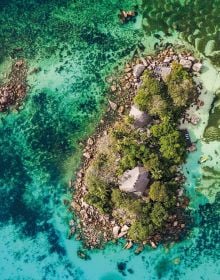 Two swimmers in turquoise sea with rocks, on cover of 'Wish I Was Here, The World's Most Extraordinary Places on and Beyond the Seashore', by Lannoo Publishers.