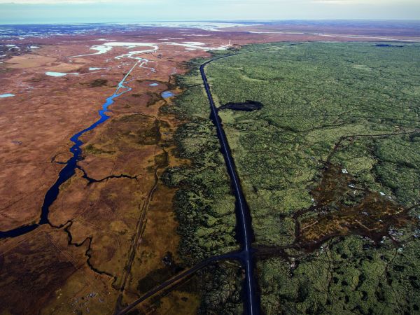 Aerial view of car on road driving through desert, on cover of 'Flatland', by Lannoo Publishers.