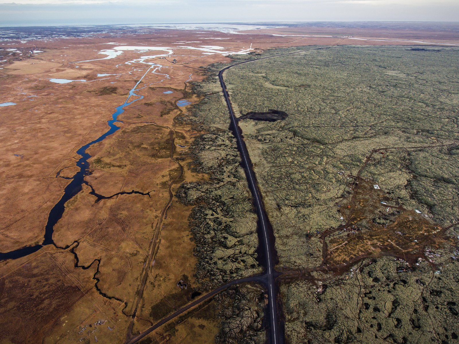 Aerial view of car on road driving through desert, on cover of 'Flatland', by Lannoo Publishers.