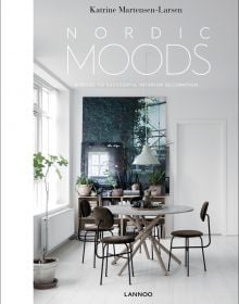 Book cover of Nordic Moods: A Guide to Successful Interior Decoration, featuring a minimalist dining interior, table and chairs, low light fixing, white walls. Published by Lannoo Publishers.