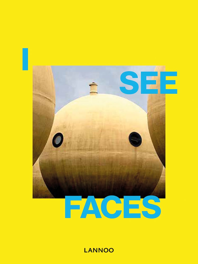 Sphere shape building structure with 2 port holes and small tower to top, resembling face, yellow cover, I SEE FACES in blue font around centre.