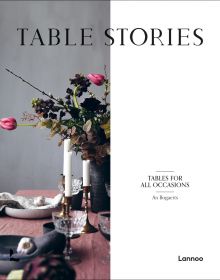 Wood table with vase of flowers, candlesticks, glasses and bowls, on cover of 'Table Stories, Tables for All Occasions', by Lannoo Publishers.