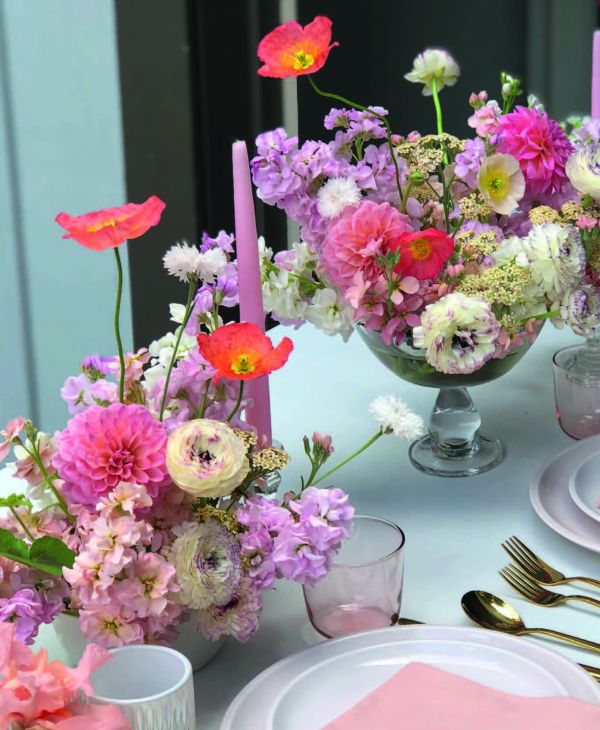 Wood table with vase of flowers, candlesticks, glasses and bowls, on cover of 'Table Stories, Tables for All Occasions', by Lannoo Publishers.