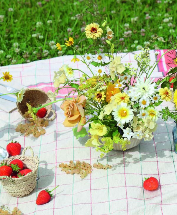 Wood table with vase of flowers, candlesticks, glasses and bowls, on cover of 'Table Stories, Tables for All Occasions', by Lannoo Publishers.