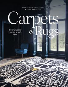 Living interior with navy wall panelling, large black and white rug, arch windows, on cover of 'Carpets & Rugs, Every home needs a soft spot', by Lannoo Publishers.