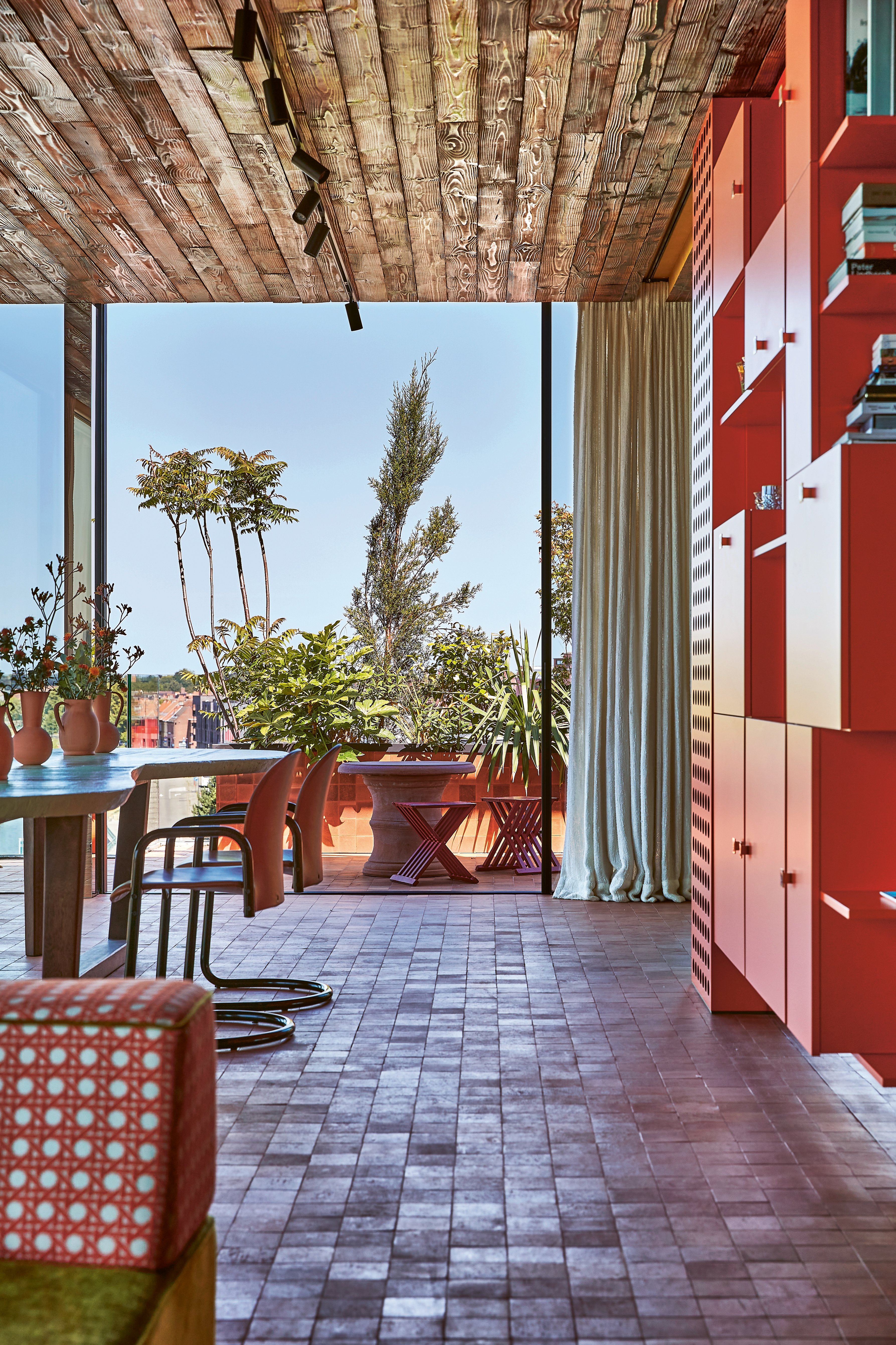 Exotic interior with bright blue wall with pink chair, yellow rug and 70s orange light fixture, on cover of 'Homes For Nomads, Interiors of the Well-Travelled', by Lannoo Publishers.