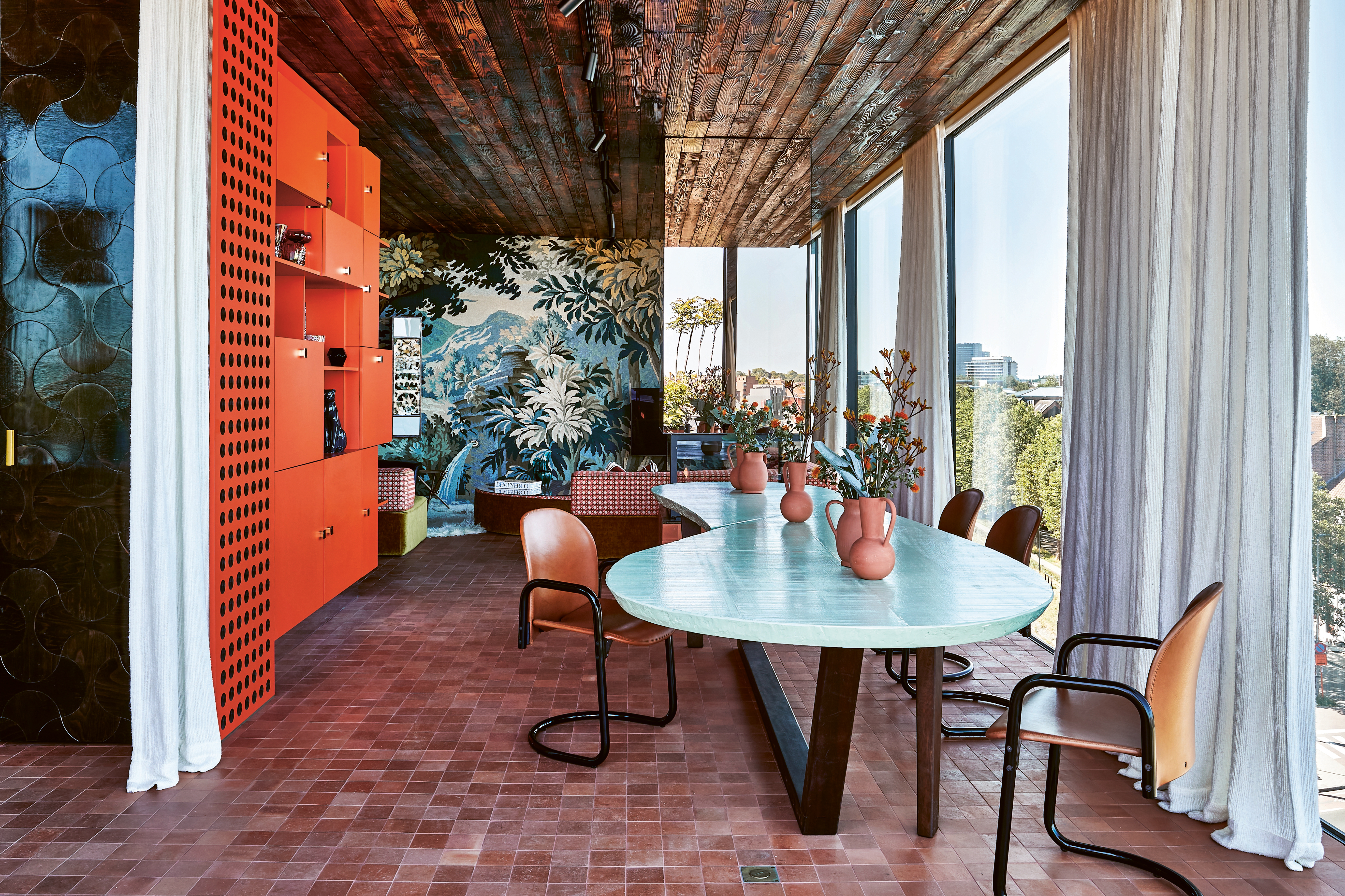 Exotic interior with bright blue wall with pink chair, yellow rug and 70s orange light fixture, on cover of 'Homes For Nomads, Interiors of the Well-Travelled', by Lannoo Publishers.