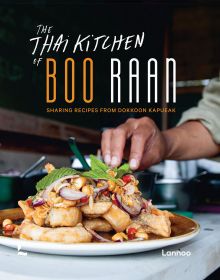 Asian style chicken dish in restaurant kitchen, chef topping with herbs, on cover of 'The Thai Kitchen of Boo Raan, Sharing Recipes From Dokkoon Kapueak', by Lannoo Publishers.