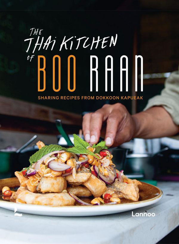 Book cover of The Thai Kitchen of Boo Raan, Sharing Recipes From Dokkoon Kapueak, with an Asian style chicken dish in restaurant kitchen, with chef topping with herbs. Published by Lannoo Publishers.