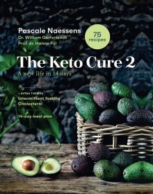 Wicker basket of green and brown skinned avocados, on wood table, on cover of 'The Keto Cure 2, A New Life in 14 Days', by Lannoo Publishers.