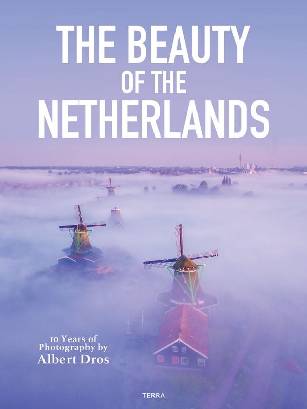 Book cover of The Beauty of the Netherlands: 10 Years of Photography by Albert Dros, with an aerial shot of an atmospheric landscape with windmills. Published by Lannoo Publishers.