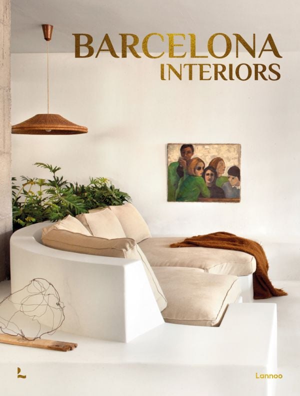 Book cover of Barcelona Interiors, with a white Mediterranean interior space with white sofa, low hanging light, and family portrait painting on wall. Published by Lannoo Publishers.
