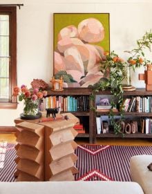 Interior living room with a bulbous terracotta armchair, large pot plant in corner, arched doors looking out into garden, on cover of 'Los Angeles Interiors', by Lannoo Publishers.